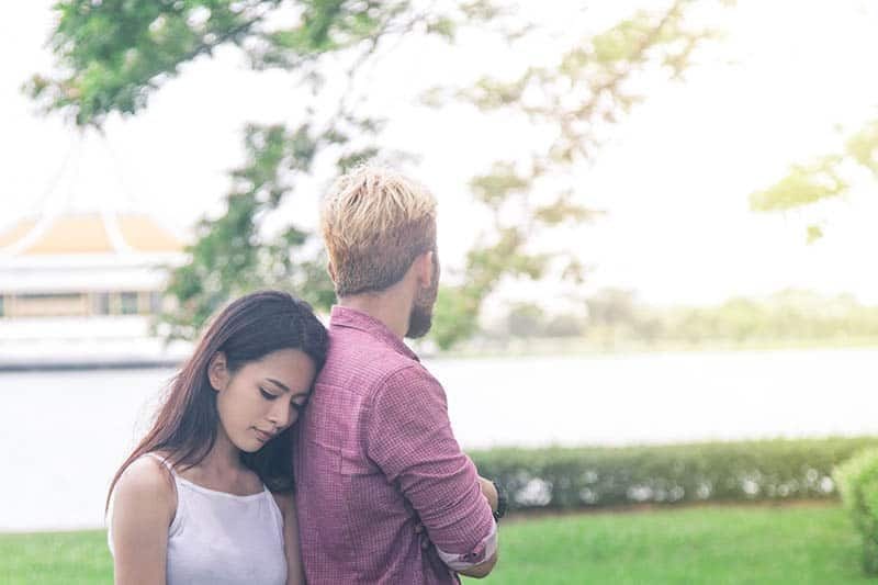 nachdenkliche Frau legt Kopf auf Mann zurück, während sie draußen steht