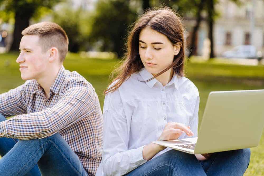 Das Mädchen sieht den Kerl traurig über die Schulter an, als sie im Gras sitzen