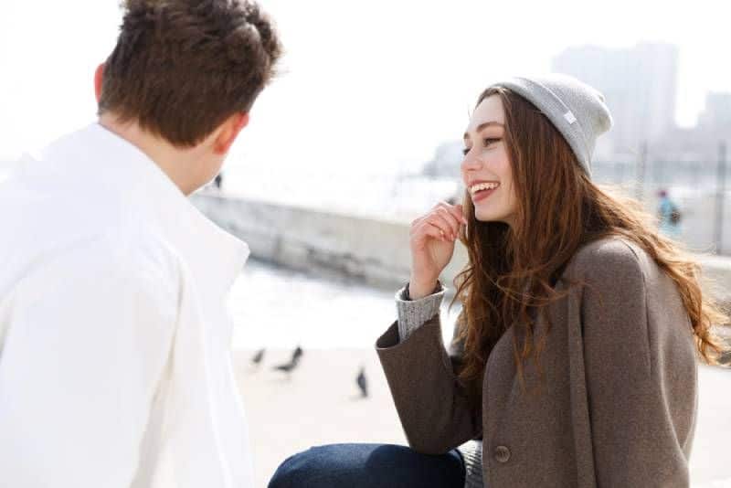 lächelndes junges Paar, das draußen sitzt und spricht