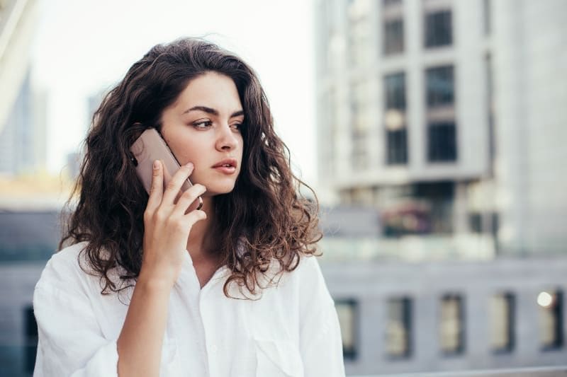 8 måter du kan ødelegge en manns interesse på uten å være klar over det ernsthafte Frau, die weißes Hemd trägt und draußen auf ihrem Telefon spricht