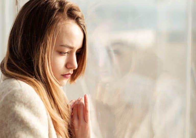 ein trauriges Mädchen, das sich gegen das Fenster lehnt