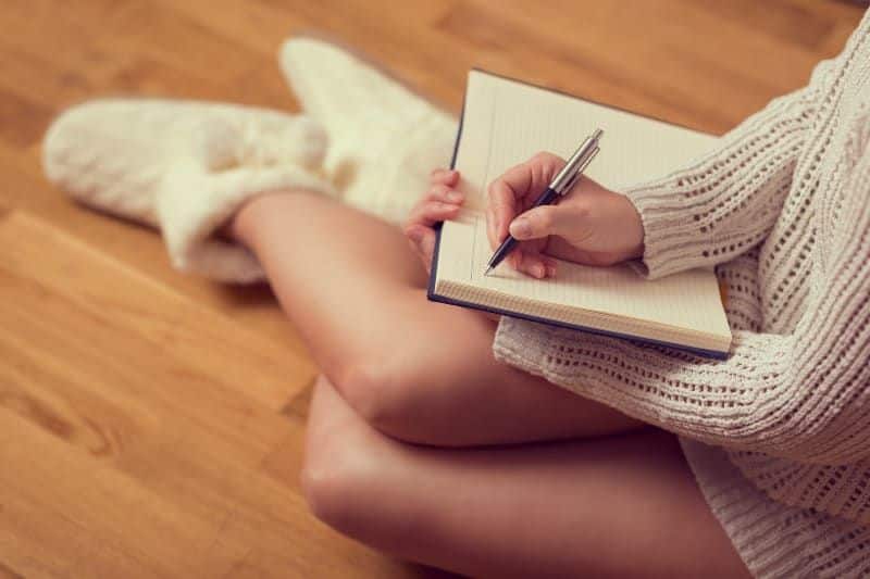 Das Mädchen sitzt auf dem Boden am Kamin und schreibt einen Brief