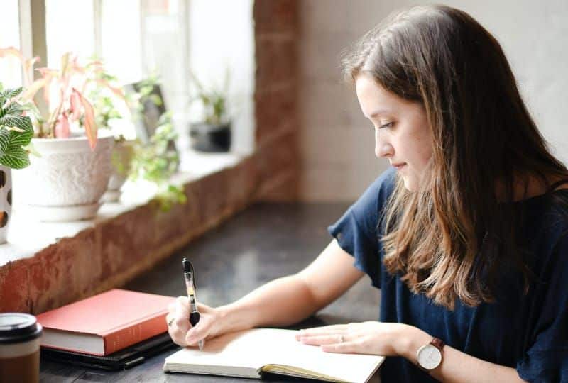 Et brev til mannen som kjemien var så utrolig god med Frau, die vor schwarzem Tisch sitzt, der auf weißem Buch nahe Fenster schreibt