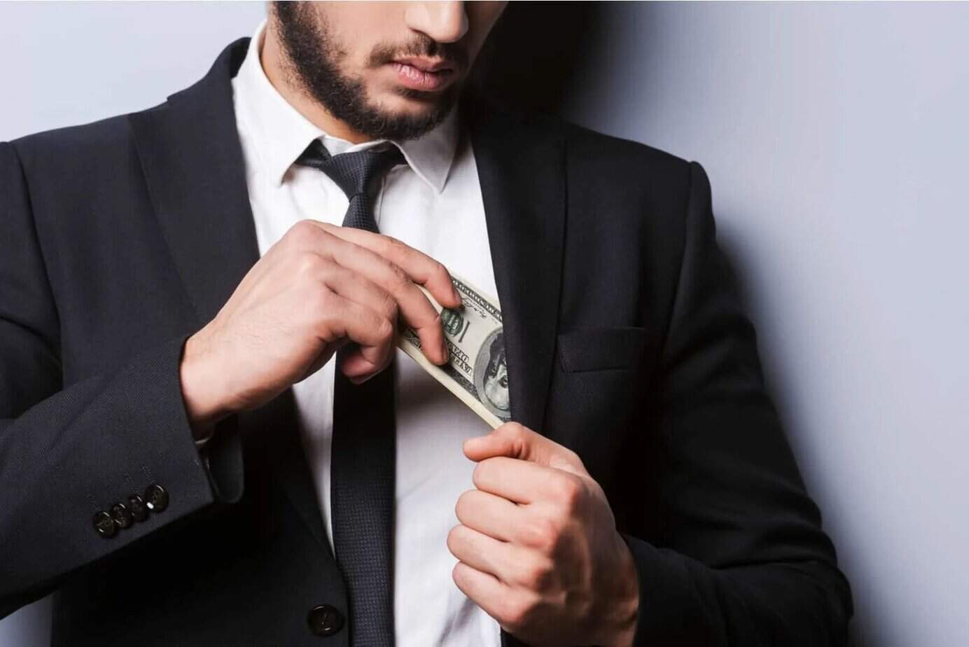 Ein gutaussehender bärtiger Mann steckt Geld in seine Jackentasche