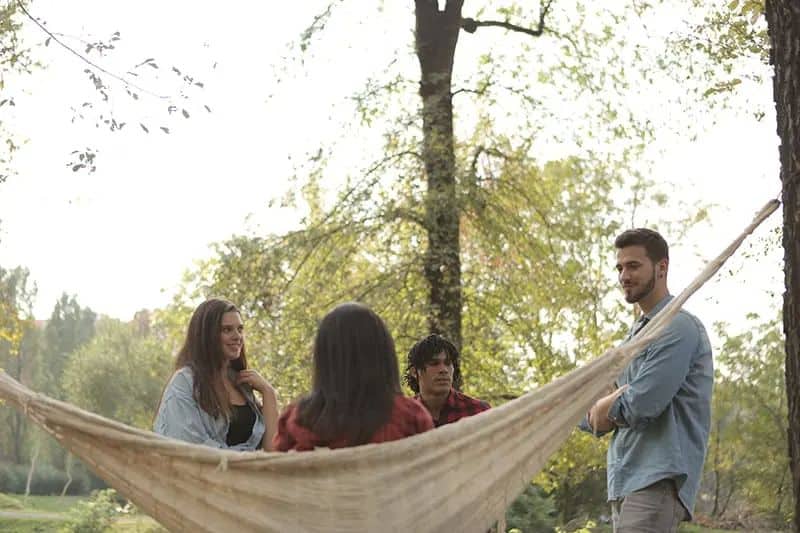 ein lächelnder Mann, der eine Frau betrachtet, die im Hummock sitzt und mit Freunden um sie herum steht