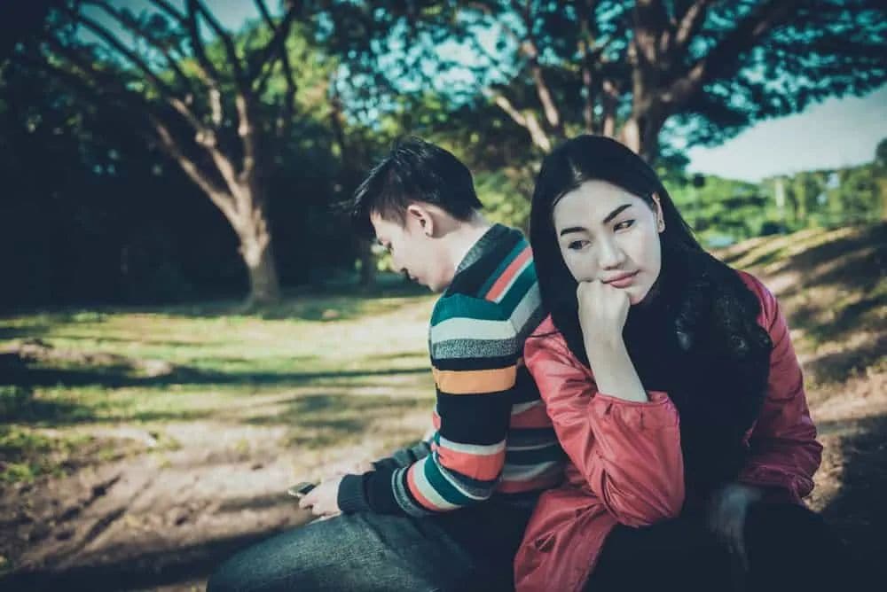 Ein Mann am Telefon und eine traurige Frau sitzen im Park