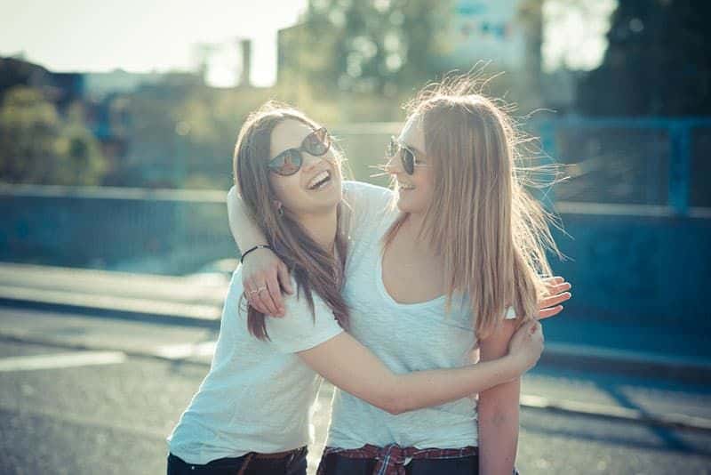 zwei lächelnde Frauen mit Brille umarmen sich