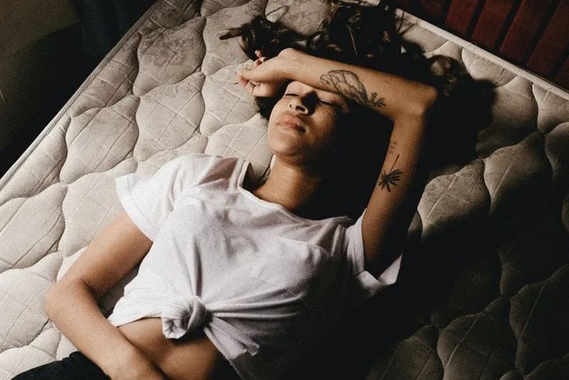 Eine schwarze Frau mit einem Tattoo auf dem Arm liegt im Bett