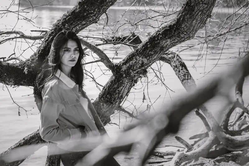 Eine Frau in Jeansjacke lehnt an einem Baum