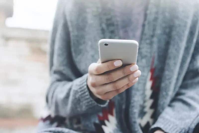 Mädchen in einem grauen Pullover, Knopf am Handy