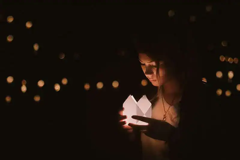 Abends steht eine Frau draußen und hält eine leuchtende Schachtel in den Händen
