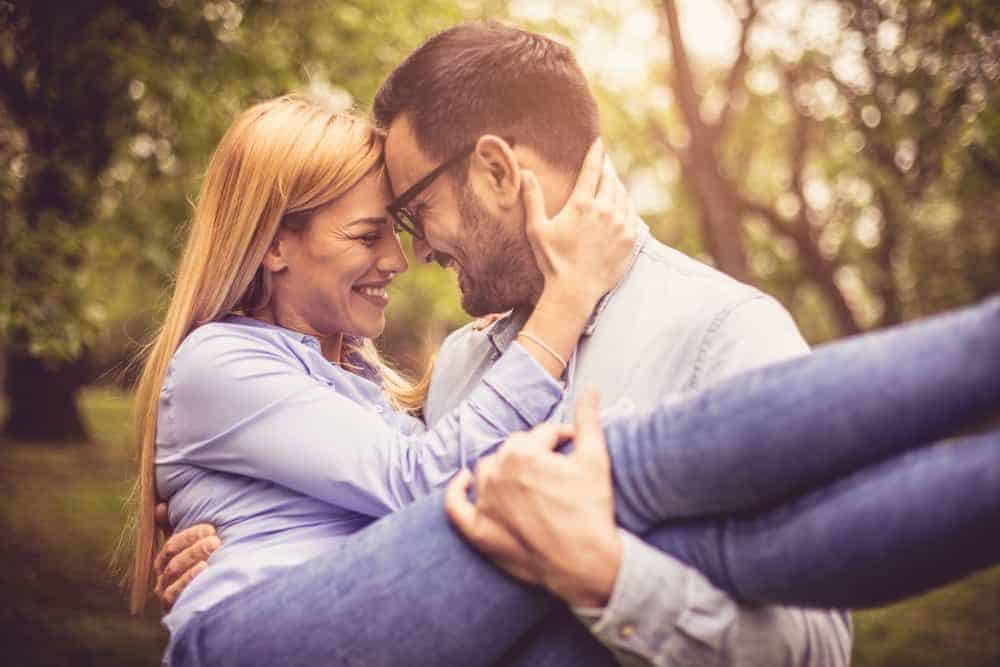 Ein glücklicher Mann im Park hält eine verliebte Frau in den Armen