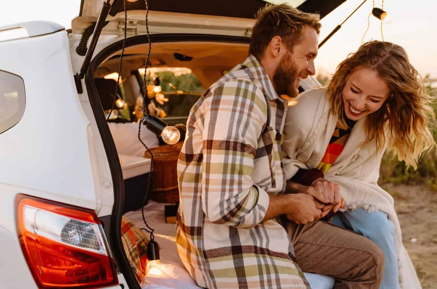 Glückliches junges Paar lächelt und sitzt zusammen im Kofferraum eines Autos