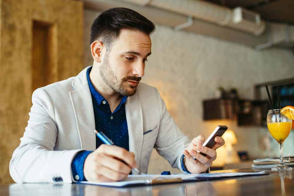 Geschäftsmann an seinem Schreibtisch schreibt SMS auf sein Handy