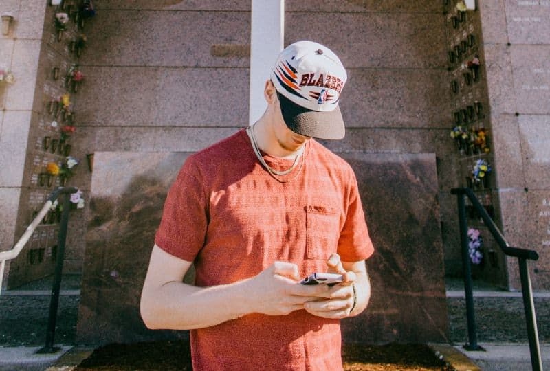 Hvis han skriver disse 10 meldingene til deg, er han en jackpot-kjæreste Mann, der Smartphone hält und nahe Kreuzstatue steht