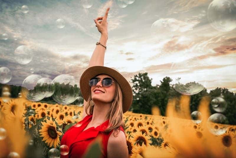 Eine glückliche Frau in einem roten Kleid mit Sonnenschirmen steht in einem Feld von Sonnenblumen