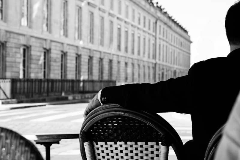 Mann in schwarzer Anzugjacke sitzt im Straßencafé