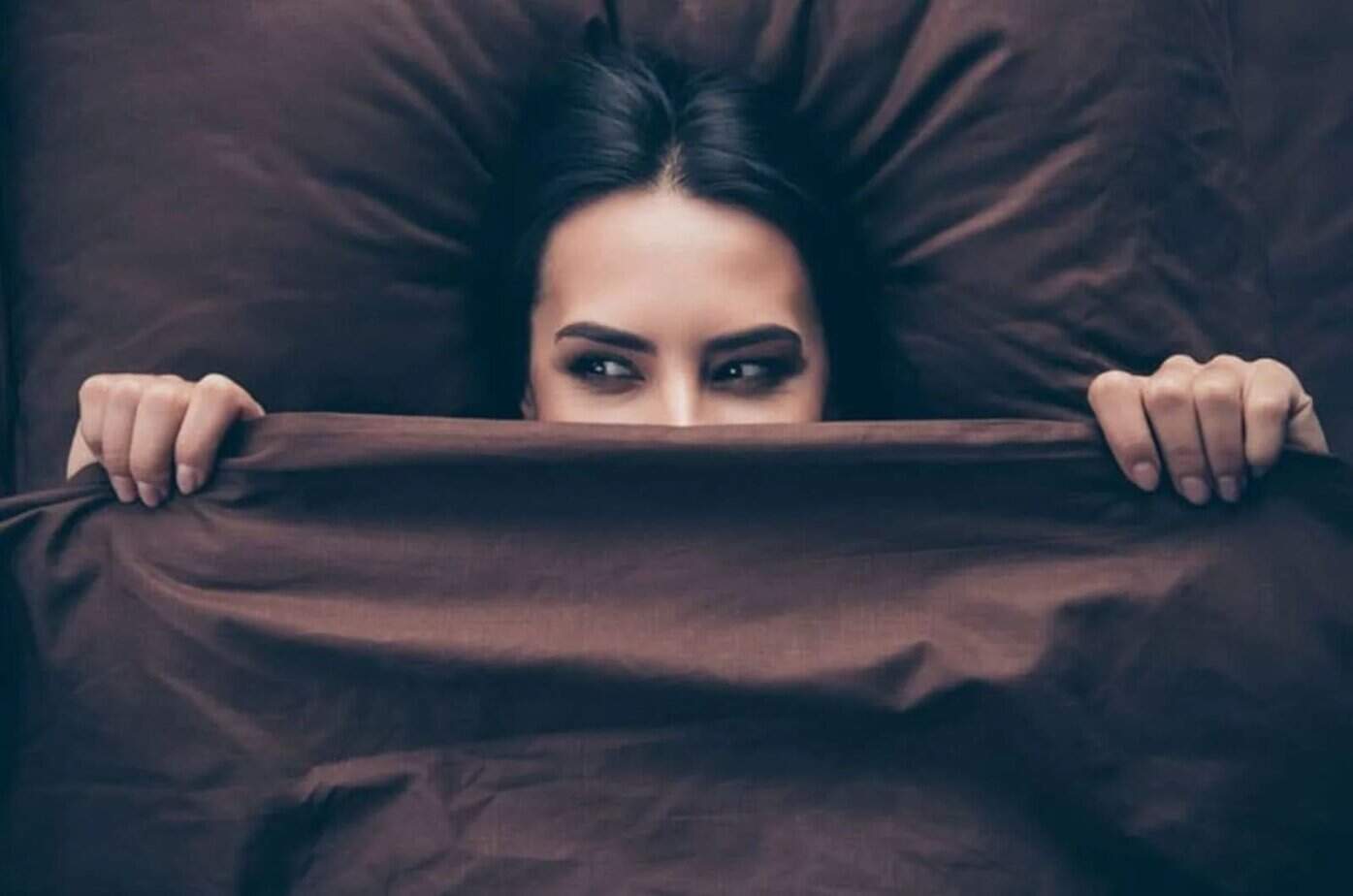 laechelnde Frau unter der Bettdecke