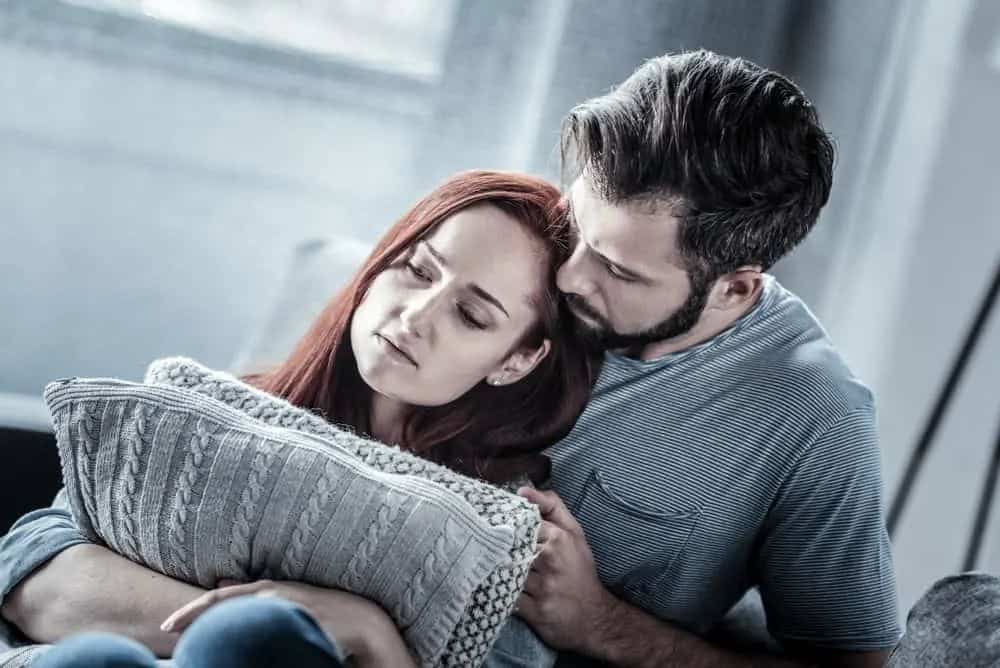 eine traurige rothaarige Frau in den Armen ihres Mannes