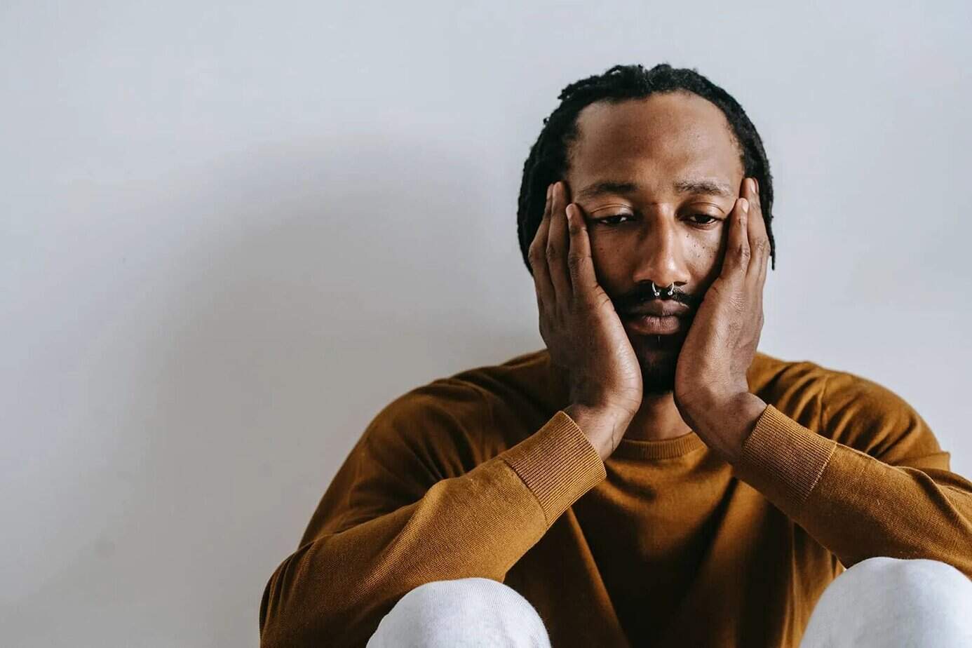unglücklicher Mann, der Gesicht mit den Händen berührt, während er auf dem Boden sitzt