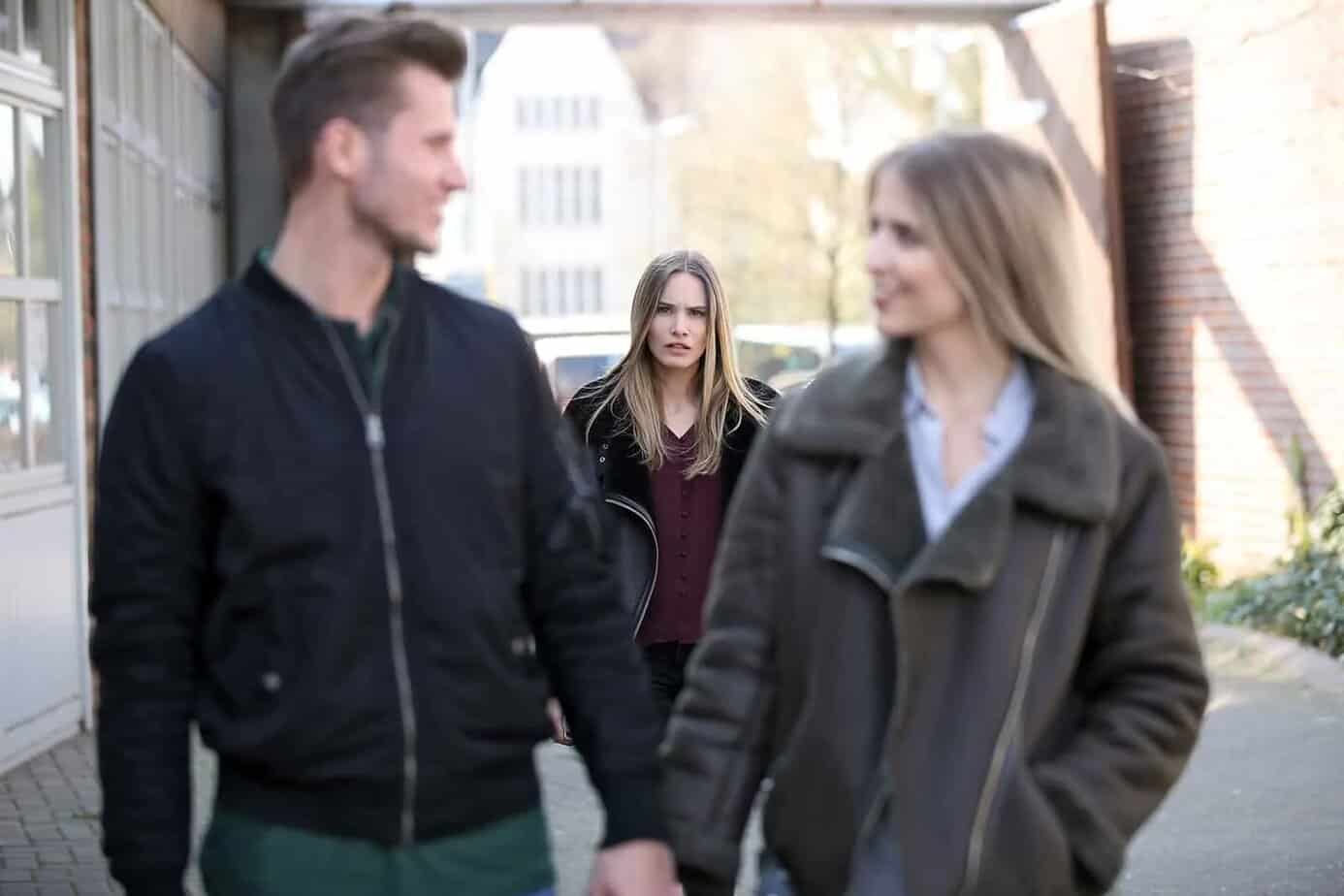 eine verwirrte Frau, die ein liebendes Paar vor sich betrachtet, während sie auf dem Bürgersteig geht