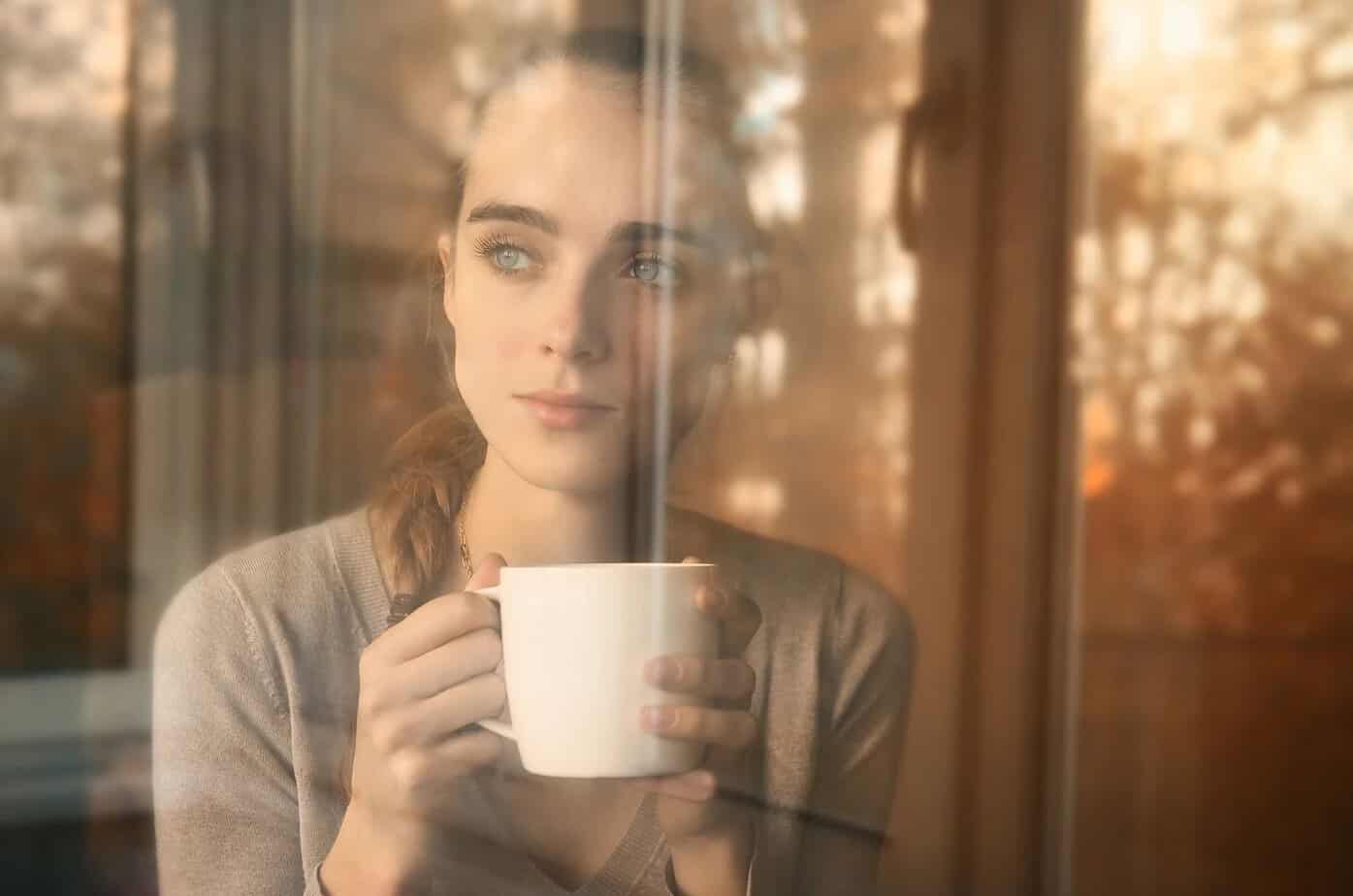 Et tegn fra universet: Kjærligheten er på vei til deg! Traurige Frau, die Kaffee trinkt und aus dem Fenster schaut